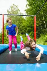 Fototapeta na wymiar Happy girls jumping high on a trampoline on a sunny day outdoors.