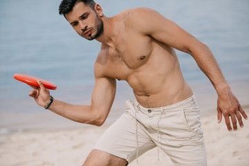 handsome young man playing with flying disc on beach