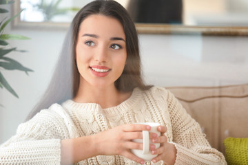 Beautiful young woman with cup of hot tea at home, view through window