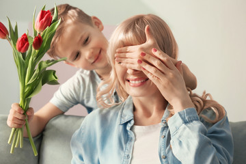 Cute little boy surprising his mother with tulip bouquet at home