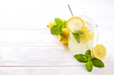 One mason jar glass of homemade refreshing lemonade with slices of organic ripe lemon, whole and halved. Non alcoholic beverage on a rustic white wooden background. Close up, top view, copy space.