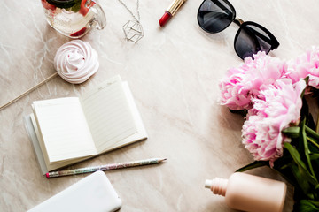 Beauty flat lay with a diary, smartphone, accessories and peonies on a marble background
