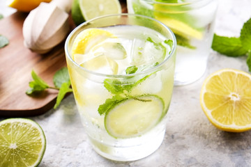 Two glasses of refreshing non alcoholic mojito lemonade drink with organic lemon, lime slices, mint leaves, straw, ice cubes on grunged grey concrete table background. Close up, top view, copy space.