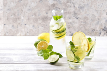 Vintage bottle with two glasses of refreshing non alcoholic mojito lemonade drink with lemon, lime slices, mint leaves, straw, ice on wooden table, concrete background. Close up, top view, copy space.