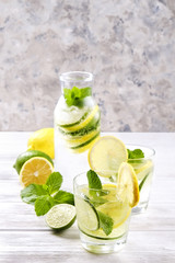 Vintage bottle with two glasses of refreshing non alcoholic mojito lemonade drink with lemon, lime slices, mint leaves, straw, ice on wooden table, concrete background. Close up, top view, copy space.