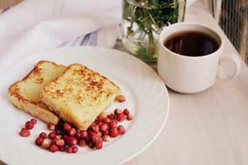 Breakfast. Croutons or toasts with berries (wild strawberry) and tea on a wooden background. Toned