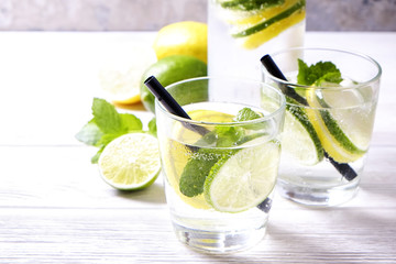 Vintage bottle with two glasses of refreshing non alcoholic mojito lemonade drink with lemon, lime slices, mint leaves, straw, ice on wooden table, concrete background. Close up, top view, copy space.