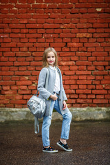 Fototapeta na wymiar portrait of little beautiful stylish kid girl with backpack near red brick wall as background