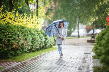 portrait of little beautiful stylish kid girl with an umbrella in the rain in city park