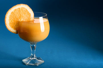 Orange juice in a glass with orange wedge on side on blue background