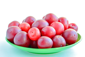 Ripe red plums in a green ceramic cup on a light background.