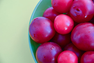 Ripe red plums in a green ceramic cup on a light background