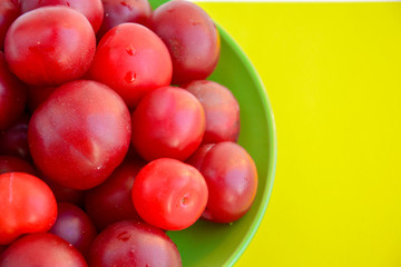 Ripe red plums in a green ceramic cup on a yellow background.