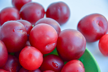 Ripe red plums in a green ceramic cup on a light background