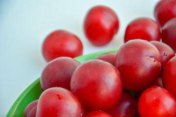 Ripe red plums in a green ceramic cup on a light background