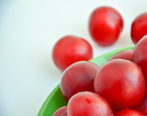 Ripe red plums in a green ceramic cup on a light background