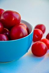 Ripe red plums in a blue ceramic cup on a light background