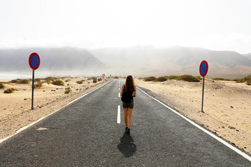 Uncertain future. Young alone woman advances with an uncertain step in empty asphalt desert road....