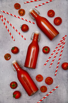 Homemade tomato juice in swing top bottles, straws and tomatoes on grey ground
