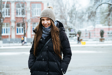 long-haired beautiful girl in a warm down jacket walking through the streets of the city in winter,...