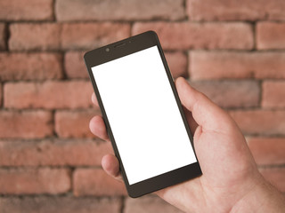 Mock up image of hand holding black mobile phone with blank white screen in portrait mode on a brick wall background