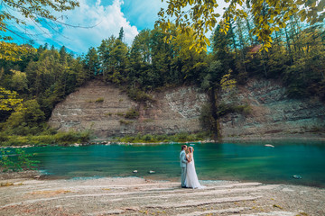 Fototapeta na wymiar Attractive Young wedding couple standing on rocks next to river variation. Bride and groom kiss each other behind the rock. Newlyweds photoshoot.