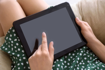 Young woman using tablet computer for online food delivery while sitting in armchair indoors
