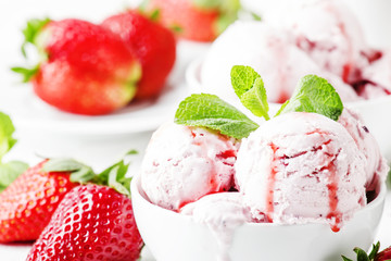 Strawberry ice cream with jam topping, decorated with green mint leaves, gray background, selective focus