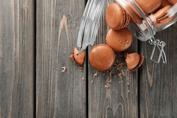 Glass jar and delicious chocolate macarons on wooden background, top view