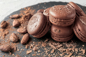 Slate plate with delicious chocolate macarons and cocoa beans, closeup