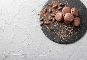 Slate plate with delicious chocolate macarons and cocoa beans on grey background, top view