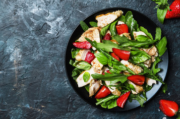 Delicious salad with arugula, strawberries and grilled chicken, top view