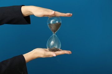 Woman holding hourglass on color background. Time management concept