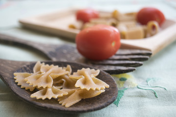 wholemeal pasta on a wooden ladle and fresh tomatoes
