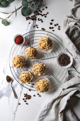 Fresh baked homemade cupcakes with coffee buttercream and caramel standing on cooling rack with eucalyptus branch and coffee beans above over white marble background. Flat lay, space