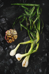 Grilled vegetables spring onion and garlic over black charcoal. Top view, space. Barbecue concept