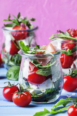 Summer salad with arugula, soft cheese, cherry tomatoes and prosciutto in glass jars, festive background, selective focus