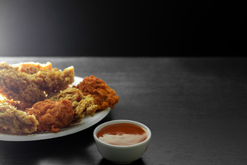 Close up and half view of light from the side. Fried chicken in dish and a cup of sauce on wooden table in the dark shadows background.