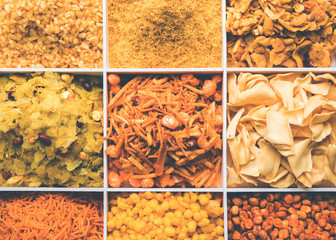 Indian Tea-time snacks like sev, chivda, farsan, mixture, boondi, bakarwadi etc served in white wooden box with cells. selective focus