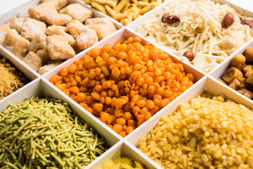 Indian Tea-time snacks like sev, chivda, farsan, mixture, boondi, bakarwadi etc served in white wooden box with cells. selective focus