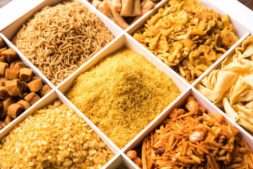Indian Tea-time snacks like sev, chivda, farsan, mixture, boondi, bakarwadi etc served in white wooden box with cells. selective focus