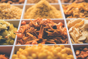 Indian Tea-time snacks like sev, chivda, farsan, mixture, boondi, bakarwadi etc served in white wooden box with cells. selective focus