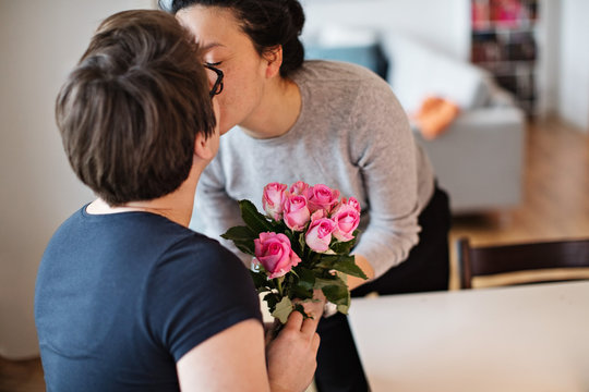 Close-up of lesbian couple kissing while holding pink roses at home