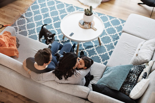 High angle view of mother kissing daughter while sitting with woman on sofa at home