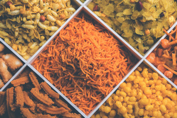 Indian Tea-time snacks like sev, chivda, farsan, mixture, boondi, bakarwadi etc served in white wooden box with cells. selective focus