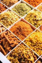 Indian Tea-time snacks like sev, chivda, farsan, mixture, boondi, bakarwadi etc served in white wooden box with cells. selective focus