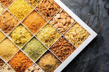 Indian Tea-time snacks like sev, chivda, farsan, mixture, boondi, bakarwadi etc served in white wooden box with cells. selective focus