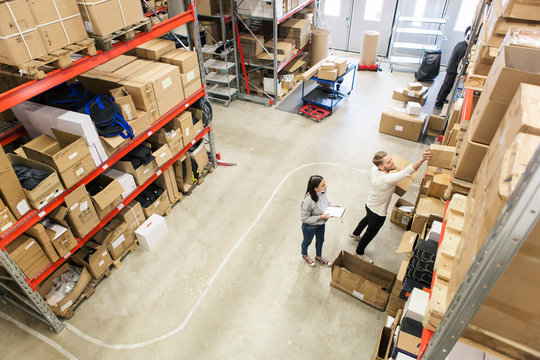 High angle view of coworkers examining boxes on rack in industry