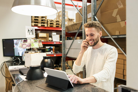 Smiling man talking on mobile phone while using digital tablet in warehouse