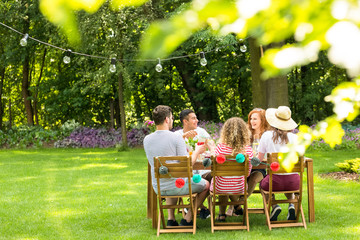 Close-up of blurred leaves in the garden with a group of friends sitting at the table and smiling...
